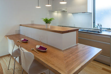 Design ideas for a modern galley eat-in kitchen in Osaka with an undermount sink, flat-panel cabinets, light wood cabinets, stainless steel benchtops, white splashback, stainless steel appliances, light hardwood floors and a peninsula.