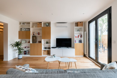 Cette image montre un salon design de taille moyenne et ouvert avec une bibliothèque ou un coin lecture, un mur blanc, parquet clair, aucune cheminée, un téléviseur indépendant et un sol marron.