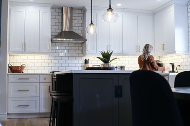 Small l-shaped light wood floor eat-in kitchen photo in Other with a farmhouse sink, shaker cabinets, white cabinets, quartz countertops, white backsplash, porcelain backsplash, stainless steel appliances, an island and white countertops