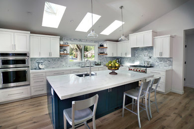 Mid-sized country light wood floor and beige floor kitchen photo in San Francisco with shaker cabinets, white cabinets, quartz countertops, gray backsplash, stone tile backsplash, stainless steel appliances, an island and white countertops