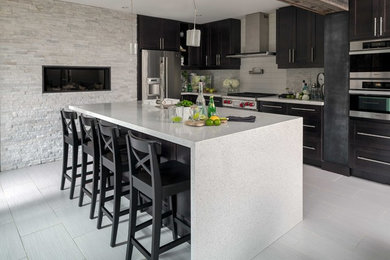 Inspiration for a large transitional l-shaped porcelain tile and gray floor open concept kitchen remodel in Toronto with an undermount sink, shaker cabinets, black cabinets, gray backsplash, subway tile backsplash, stainless steel appliances and an island