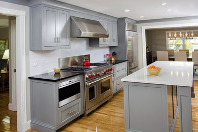 Contemporary kitchen pantry in Boston with an undermount sink, beaded inset cabinets, grey cabinets, solid surface benchtops, white splashback, subway tile splashback, stainless steel appliances, light hardwood floors and with island.