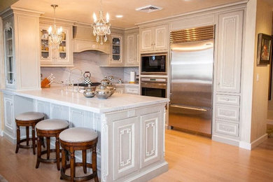 Inspiration for a mid-sized timeless light wood floor and brown floor kitchen remodel in San Diego with white cabinets, marble countertops, stone slab backsplash, stainless steel appliances and a peninsula