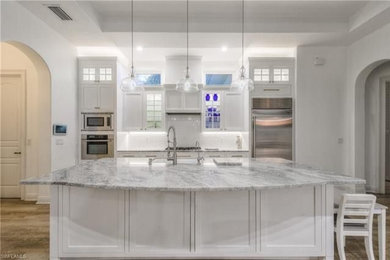 Example of a huge transitional single-wall light wood floor and brown floor open concept kitchen design in Baltimore with an undermount sink, shaker cabinets, white cabinets, quartzite countertops, white backsplash, ceramic backsplash, stainless steel appliances, an island and multicolored countertops