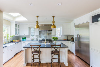 This is an example of a traditional u-shaped kitchen in San Francisco with a farmhouse sink, recessed-panel cabinets, white cabinets, white splashback, subway tile splashback, stainless steel appliances, dark hardwood floors and with island.