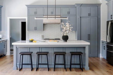 Eat-in kitchen - large transitional medium tone wood floor eat-in kitchen idea in Chicago with shaker cabinets, gray cabinets, white backsplash, ceramic backsplash, stainless steel appliances and an island
