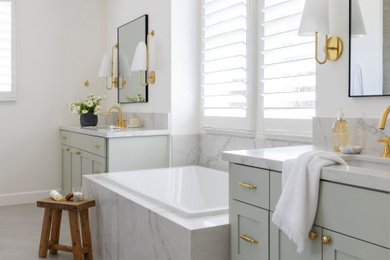 Inspiration for a transitional light wood floor, beige floor and double-sink drop-in bathtub remodel with shaker cabinets, gray cabinets, white walls, an undermount sink, white countertops and a built-in vanity