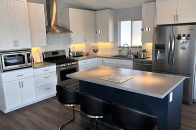 Inspiration for a mid-sized coastal l-shaped laminate floor and gray floor open concept kitchen remodel in San Luis Obispo with an undermount sink, shaker cabinets, white cabinets, quartz countertops, white backsplash, ceramic backsplash, stainless steel appliances, an island and gray countertops