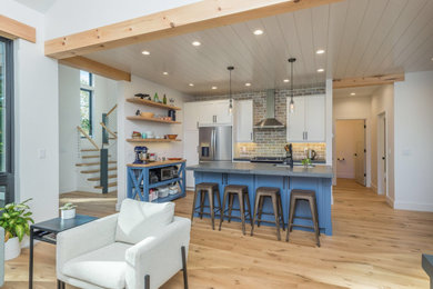 Example of a mid-sized transitional l-shaped light wood floor and brown floor open concept kitchen design in Other with an undermount sink, recessed-panel cabinets, blue cabinets, concrete countertops, beige backsplash, brick backsplash, stainless steel appliances, an island and gray countertops