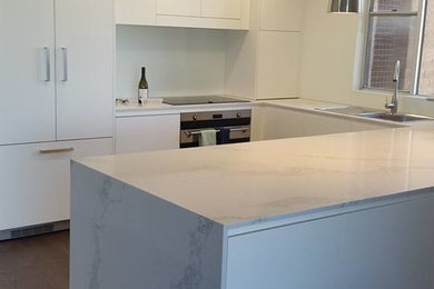 This is an example of a mid-sized modern u-shaped eat-in kitchen in Sydney with a drop-in sink, white cabinets, white splashback, glass sheet splashback, stainless steel appliances and laminate floors.