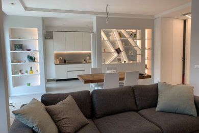 This is an example of a large contemporary open concept living room in Rome with a library, white walls, porcelain floors, a corner fireplace, a plaster fireplace surround and grey floor.
