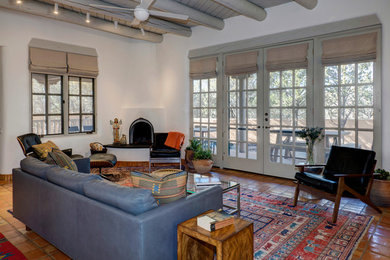 Photo of a mid-sized eclectic open concept living room in Albuquerque with white walls, terra-cotta floors, a corner fireplace, a plaster fireplace surround and orange floor.