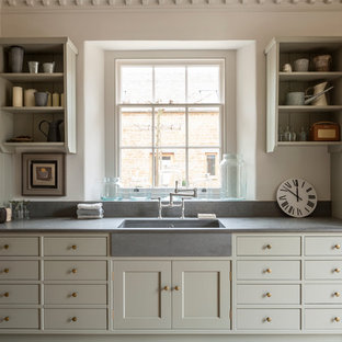 グロスタシャーの中サイズのカントリー風おしゃれなランドリールーム (落し込みパネル扉のキャビネット、ライムストーンカウンター、白い壁、ライムストーンの床、グレーのキャビネット、シングルシンク) の写真