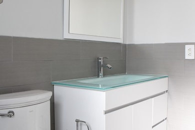 Inspiration for a modern gray floor bathroom remodel in Miami with flat-panel cabinets, white cabinets, a one-piece toilet, white walls, an integrated sink and glass countertops