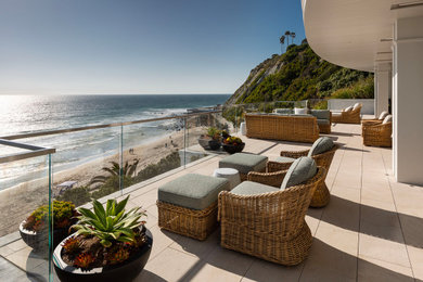 Example of a beach style glass railing balcony design in Orange County with a roof extension