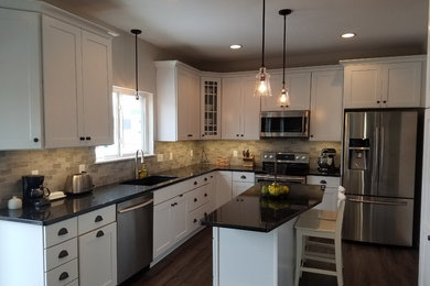 Kitchen - mid-sized traditional vinyl floor kitchen idea in Milwaukee with a double-bowl sink, shaker cabinets, white cabinets, granite countertops, gray backsplash, travertine backsplash, stainless steel appliances and an island