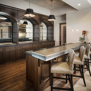 フェニックスの巨大な地中海スタイルのおしゃれなウェットバー (ドロップインシンク、落し込みパネル扉のキャビネット、濃色木目調キャビネット、亜鉛製カウンター、ベージュの床、グレーのキッチンカウンター) の写真