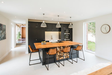 This is an example of a transitional single-wall kitchen in Other with shaker cabinets, black cabinets, wood benchtops, white splashback, black appliances, with island, white floor and brown benchtop.