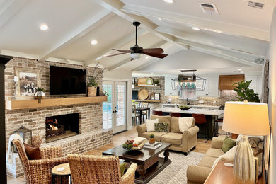 Example of a classic open concept medium tone wood floor, brown floor and vaulted ceiling family room design in Dallas with white walls, a standard fireplace, a brick fireplace and a wall-mounted tv