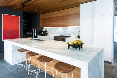 This is an example of a large contemporary single-wall kitchen pantry in Melbourne with a double-bowl sink, medium wood cabinets, marble benchtops, multi-coloured splashback, marble splashback, stainless steel appliances and with island.