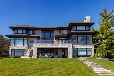 Large transitional beige three-story stone house exterior photo in Detroit with a hip roof and a shingle roof