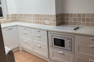 This is an example of a small contemporary l-shaped kitchen/diner in Other with a built-in sink, shaker cabinets, white cabinets, laminate countertops, ceramic splashback, integrated appliances, ceramic flooring, no island and white worktops.