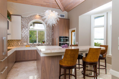 Mid-sized contemporary l-shaped kitchen in Tampa with an undermount sink, flat-panel cabinets, light wood cabinets, solid surface benchtops, brown splashback, glass tile splashback, black appliances, marble floors, with island and beige floor.