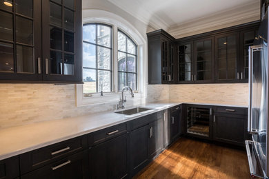 Example of a mid-sized l-shaped medium tone wood floor and brown floor home bar design in Philadelphia with a drop-in sink, glass-front cabinets, black cabinets, granite countertops, multicolored backsplash and white countertops