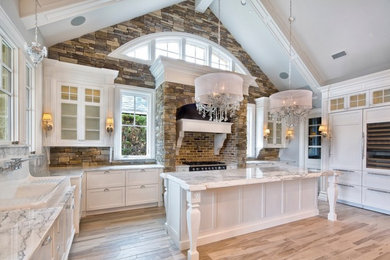 Large traditional u-shaped eat-in kitchen in Dallas with a farmhouse sink, recessed-panel cabinets, white cabinets, marble benchtops, multi-coloured splashback, stone tile splashback, panelled appliances, light hardwood floors and with island.
