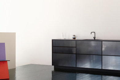 Imagen de cocina lineal industrial con puertas de armario negras, encimera de laminado y encimeras negras