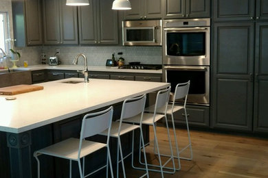 Transitional u-shaped medium tone wood floor eat-in kitchen photo in San Diego with a drop-in sink, raised-panel cabinets, black cabinets, laminate countertops, white backsplash, stainless steel appliances and an island