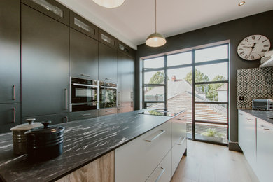 Photo of a medium sized contemporary galley open plan kitchen in Cardiff with an integrated sink, flat-panel cabinets, composite countertops, multi-coloured splashback, cement tile splashback, stainless steel appliances, medium hardwood flooring, an island, black worktops, black cabinets, beige floors and a feature wall.