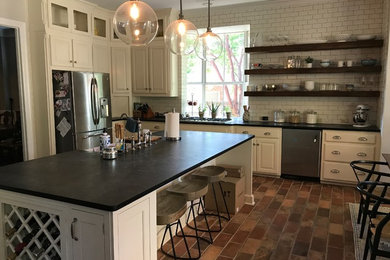 Eat-in kitchen - large country l-shaped brick floor and multicolored floor eat-in kitchen idea in Dallas with a farmhouse sink, white cabinets, white backsplash, subway tile backsplash, stainless steel appliances, an island and raised-panel cabinets