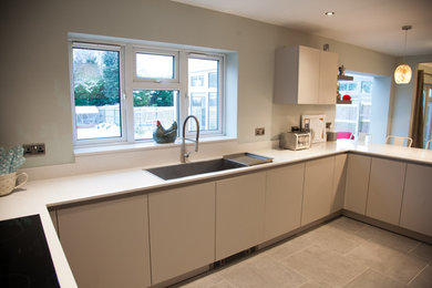 This is an example of a large contemporary u-shaped open plan kitchen in West Midlands with a built-in sink, flat-panel cabinets, white cabinets, quartz worktops, white splashback, stone slab splashback, stainless steel appliances, porcelain flooring, a breakfast bar and grey floors.