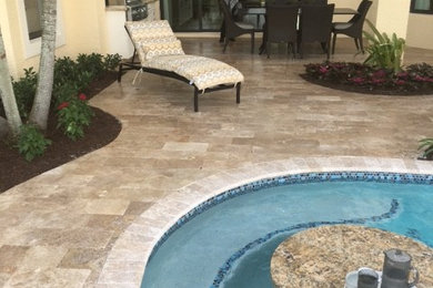 This is an example of a large contemporary backyard custom-shaped pool in Miami with natural stone pavers.