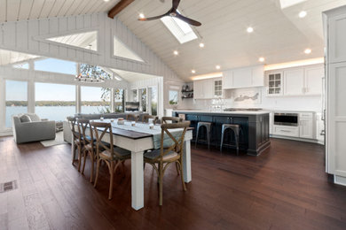 Open concept kitchen - large coastal u-shaped dark wood floor, brown floor and wood ceiling open concept kitchen idea in Milwaukee with a farmhouse sink, shaker cabinets, white cabinets, quartz countertops, white backsplash, subway tile backsplash, stainless steel appliances, an island and white countertops