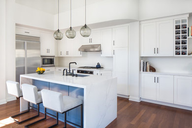 Photo of a contemporary kitchen in Los Angeles with a drop-in sink, flat-panel cabinets, white cabinets, white splashback, stainless steel appliances, medium hardwood floors, with island and brown floor.