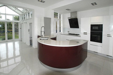 Photo of a large contemporary u-shaped open plan kitchen in London with an integrated sink, flat-panel cabinets, red cabinets, quartz worktops, white splashback, glass sheet splashback, black appliances, porcelain flooring, no island, grey floors and white worktops.