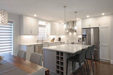 Inspiration for a mid-sized transitional l-shaped dark wood floor and brown floor eat-in kitchen remodel in Montreal with a drop-in sink, shaker cabinets, white cabinets, quartz countertops, white backsplash, mosaic tile backsplash, stainless steel appliances, an island and white countertops