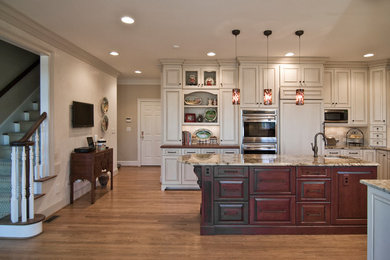 Large elegant u-shaped light wood floor eat-in kitchen photo in Charlotte with an undermount sink, white cabinets, granite countertops, beige backsplash, stone tile backsplash, paneled appliances, an island and raised-panel cabinets