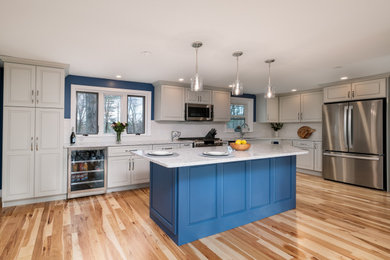 Eat-in kitchen - mid-sized transitional l-shaped light wood floor eat-in kitchen idea in Boston with a single-bowl sink, raised-panel cabinets, gray cabinets, quartz countertops, white backsplash, ceramic backsplash, stainless steel appliances, an island and white countertops