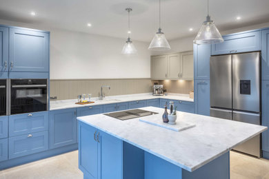 Large coastal l-shaped kitchen/diner in Other with an integrated sink, shaker cabinets, blue cabinets, composite countertops, beige splashback, black appliances, porcelain flooring, an island, beige floors and white worktops.