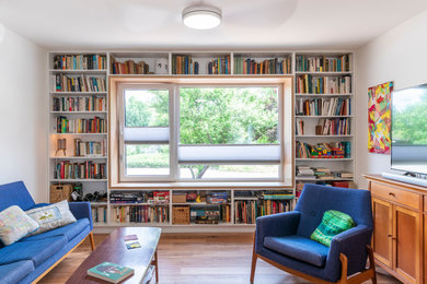 Modelo de biblioteca en casa abierta contemporánea pequeña con paredes blancas, suelo de madera en tonos medios, televisor independiente y suelo marrón