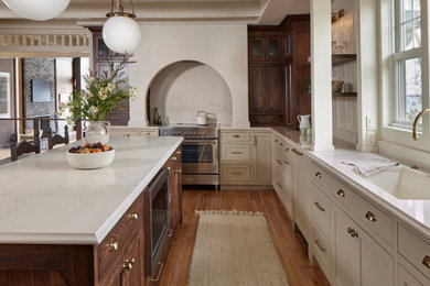 Transitional medium tone wood floor and brown floor enclosed kitchen photo in Minneapolis with an undermount sink, raised-panel cabinets, brown cabinets, quartz countertops, white backsplash, quartz backsplash, stainless steel appliances, an island and white countertops