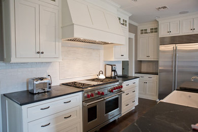 Inspiration for a large timeless l-shaped dark wood floor kitchen pantry remodel in New York with a farmhouse sink, shaker cabinets, white cabinets, soapstone countertops, white backsplash, ceramic backsplash, stainless steel appliances and an island
