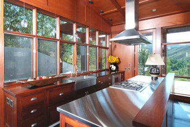 Example of a minimalist medium tone wood floor kitchen design in Seattle with a farmhouse sink, medium tone wood cabinets, stainless steel appliances and an island