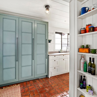На фото: линейная кухня среднего размера в стиле кантри с кладовкой, фасадами в стиле шейкер, синими фасадами, кирпичным полом и серой столешницей с