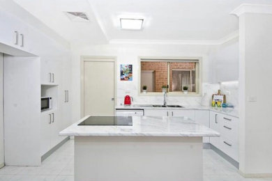This is an example of a large contemporary u-shaped open plan kitchen in Sydney with a double-bowl sink, flat-panel cabinets, white cabinets, laminate benchtops, white splashback, ceramic splashback, stainless steel appliances, ceramic floors, with island and white floor.