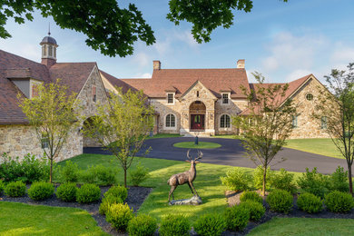 This is an example of a large country house exterior in Philadelphia with stone veneer, a gable roof and a tile roof.
