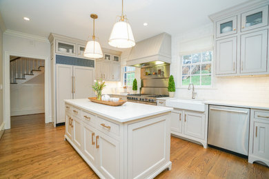 This is an example of a mid-sized traditional galley eat-in kitchen in Other with a farmhouse sink, flat-panel cabinets, white cabinets, marble benchtops, white splashback, ceramic splashback, stainless steel appliances, medium hardwood floors, multiple islands and brown floor.